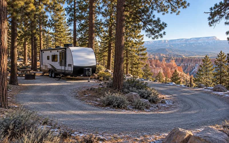 A travel trailer parked in a pine-shaded campground loop on the rim above Bryce hoodoos