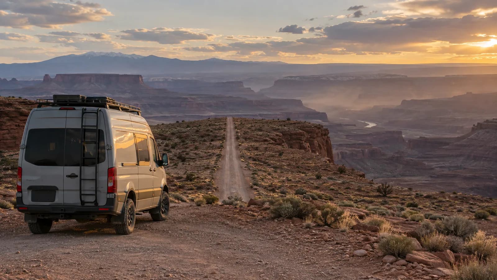 A short camper van at the start of an unpaved gravel road running out across a mesa top