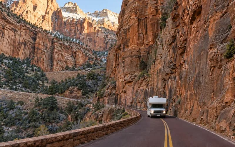 A motorhome on a narrow canyon road below sheer sandstone walls, showing how little clearance the route allows