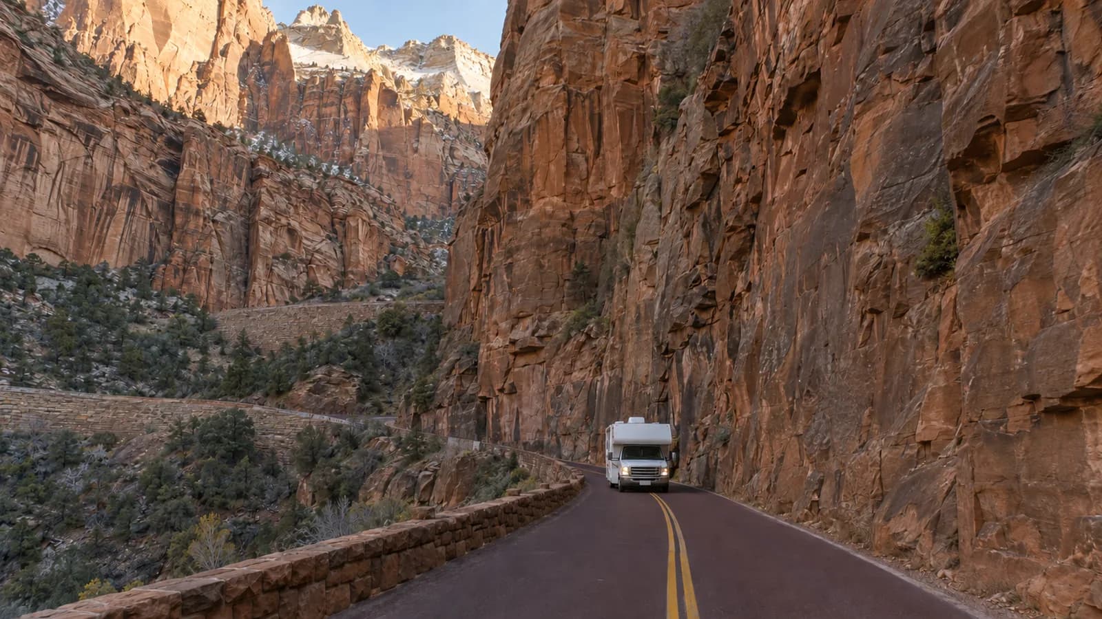A motorhome on a narrow canyon road below sheer sandstone walls, showing how little clearance the route allows